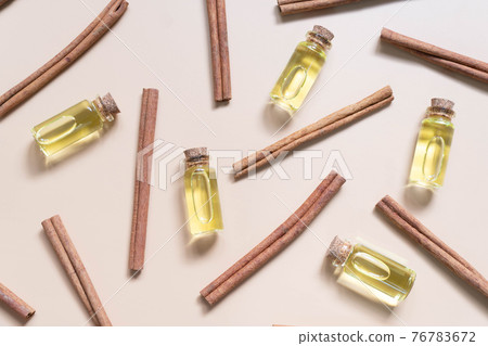 Cinnamon essential oil bottles with cinnamon sticks on brown background. Cinnamon bark oil used in aromatherapy, cosmetic and medicine. Top view. Flat lay. Cinnamon essential oil bottles with cinnamon sticks on brown background. Cinnamon bark oil used in aromatherapy, cosmetic and medicine. Top view. Flat lay. 76783672