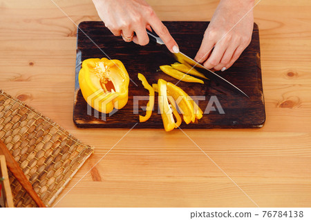 Woman cuts yellow bell pepper for salad on wooden table 76784138