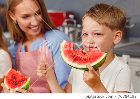 Little boy biting a slice of watermelon in kitchen 76784182