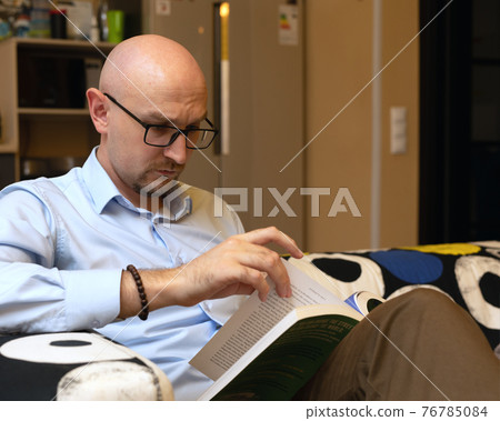 Thoughtful male person reading book while sitting in modern loft interior 76785084