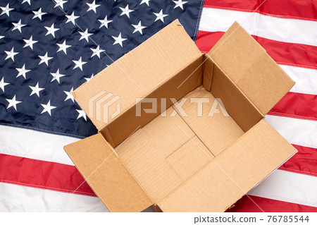 USA flag with open shipping box. Delivery from the USA. Empty postal box on American flag 76785544