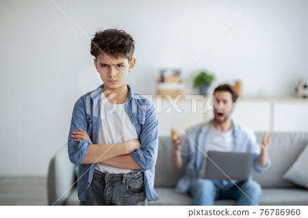 Family problems during quarantine. Angry father shouting at son while sitting with laptop computer on sofa at home 76786960