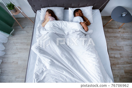 Millennial multiracial couple turning away from each other, sleeping in bed at home, top view 76786962