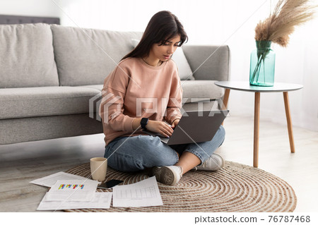 Focused woman working on laptop sitting on floor at home 76787468