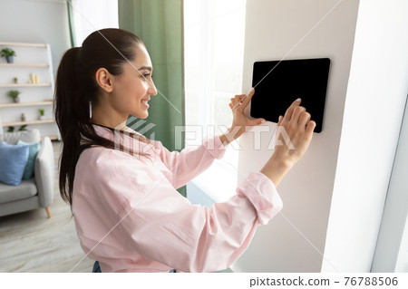 Woman using smart wall home control system in living room Woman using smart wall home control system in living room 76788506
