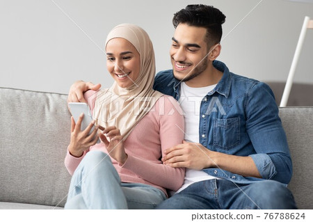 Joyful muslim couple watching photos on mobile phone together Joyful muslim couple watching photos on mobile phone together 76788624