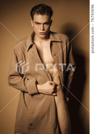 Muscle strong beautiful stripped male model in beige coat on beige isolated font background Muscle strong beautiful stripped male model in beige coat on beige isolated font background 76793696