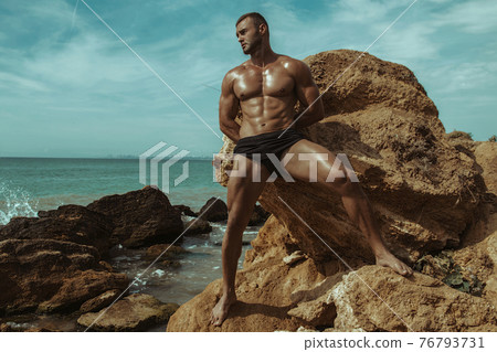 Strong face muscle male model on the nature background with sand stones and water on the beach on the sunset Strong face muscle male model on the nature background with sand stones and water on the beach on the sunset 76793731