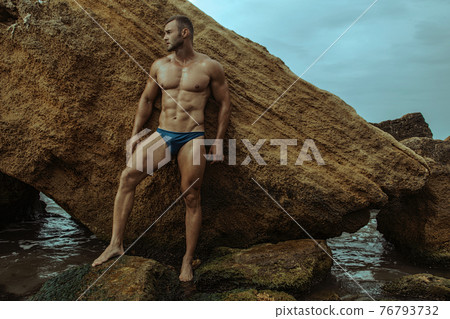 Strong face muscle male model on the nature background with sand stones and water on the beach on the sunset Strong face muscle male model on the nature background with sand stones and water on the beach on the sunset 76793732