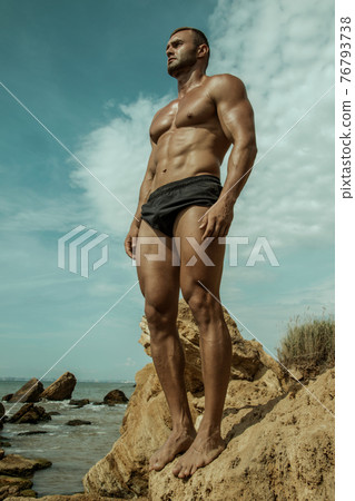 Strong face muscle male model on the nature background with sand stones and water on the beach on the sunset Strong face muscle male model on the nature background with sand stones and water on the beach on the sunset 76793738