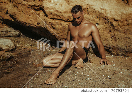 Strong face sexy sport male model in wet blue jeans in sea water on stones background Strong face sexy sport male model in wet blue jeans in sea water on stones background 76793794