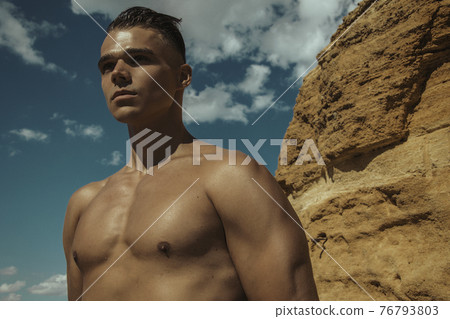 Strong face sexy sport male model in wet blue jeans in sea water on stones background Strong face sexy sport male model in wet blue jeans in sea water on stones background 76793803
