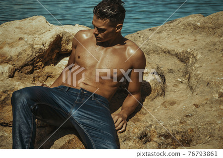 Strong face sexy sport male model in wet blue jeans in sea water on stones background Strong face sexy sport male model in wet blue jeans in sea water on stones background 76793861