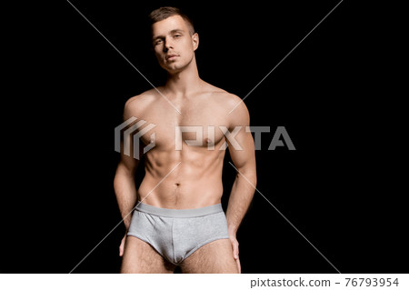 Strong stripped muscle male model in gray underwear on black isolated font background Strong stripped muscle male model in gray underwear on black isolated font background 76793954