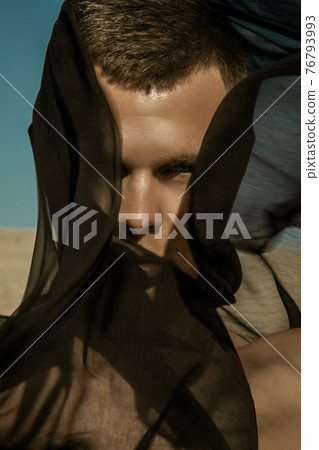 Guy with black scarf and wind on sky background in dessert Guy with black scarf and wind on sky background in dessert 76793993