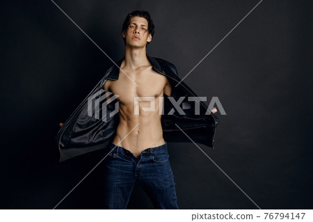 Male model in denim blue jeans and black leather jacket on black background 76794147