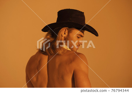 Sexy sport muscle strongface blond guy with long hair in cowbow hat on orange yellow isolated font background Sexy sport muscle strongface blond guy with long hair in cowbow hat on orange yellow isolated font background 76794344