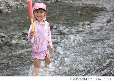 Toddler (5-year-old child) playing in the river with a water gun Toddler (5-year-old child) playing in the river with a water gun 76794874