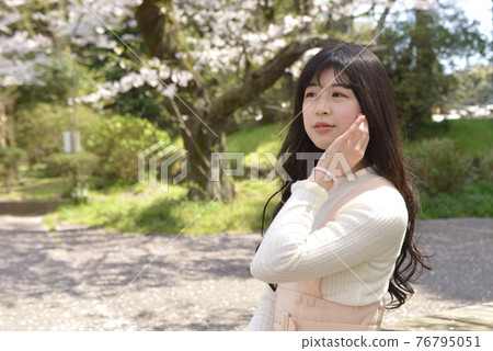 微笑在櫻花公園的一位年輕美麗的婦女 76795051