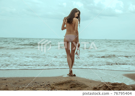 Stunning beautiful dark hair girl stripped in swimsuit on the sunset at he beach Stunning beautiful dark hair girl stripped in swimsuit on the sunset at he beach 76795404