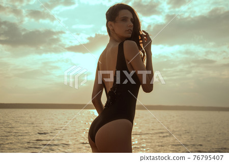 Stunning beautiful dark hair girl stripped in swimsuit on the sunset at he beach Stunning beautiful dark hair girl stripped in swimsuit on the sunset at he beach 76795407