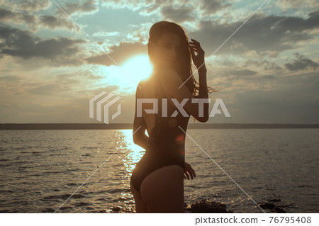 Stunning beautiful dark hair girl stripped in swimsuit on the sunset at he beach Stunning beautiful dark hair girl stripped in swimsuit on the sunset at he beach 76795408