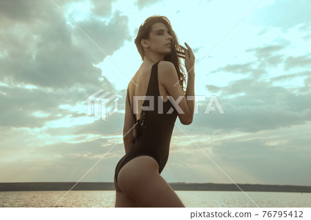 Stunning beautiful dark hair girl stripped in swimsuit on the sunset at he beach Stunning beautiful dark hair girl stripped in swimsuit on the sunset at he beach 76795412
