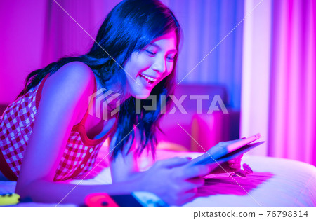 Young asian woman is using virtual reality headset. Neon light studio portrait. Concept of virtual reality, simulation, gaming and future technology.Asian woman play game in bedroom. Young asian woman is using virtual reality headset. Neon light studio portrait. Concept of virtual reality, simulation, gaming and future technology.Asian woman play game in bedroom. 76798314