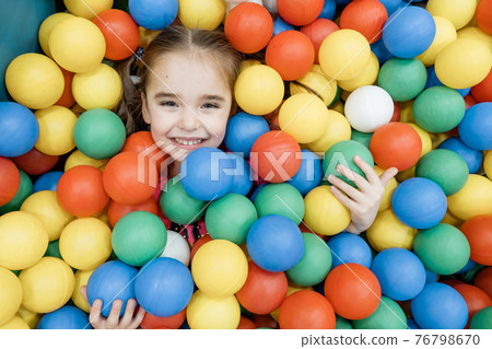 a child in the children's playroom. The girl is having fun among the colorful balls. Dry Pool Party 76798670