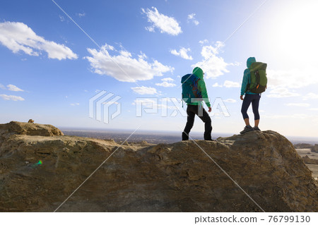 Two successful women backpackers standing on the top frozen soil hill top Two successful women backpackers standing on the top frozen soil hill top 76799130