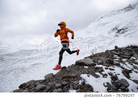 Woman trail runner cross country running down hill from winter snow mountain top 76799297