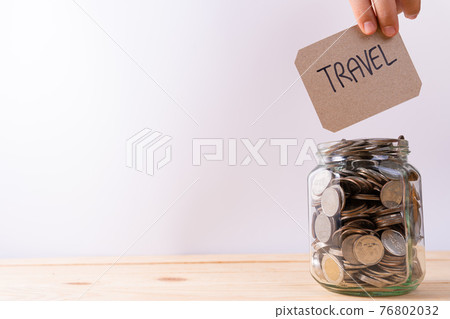 Jar full of coins with travel word paper on wooden table isolated grey background. Saving money and investment concept. 76802032