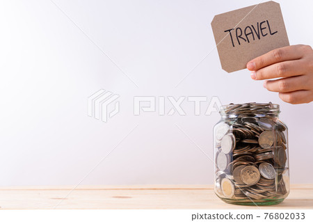 Jar full of coins with travel word paper on wooden table isolated grey background. Saving money and investment concept. 76802033
