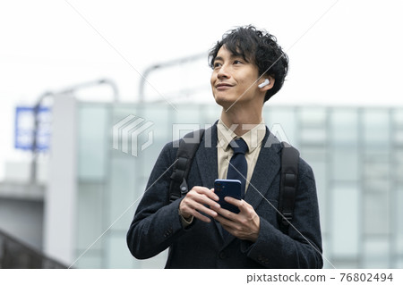 A man in his early 30s wearing headphones with a smartphone 76802494