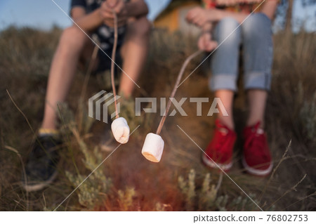 two children, a boy and a girl are holding on their sticks white marshmallows over a bonfire, concept, hike, camping holiday, sweet supper, close-up of shooting two children, a boy and a girl are holding on their sticks white marshmallows over a bonfire, concept, hike, camping holiday, sweet supper, close-up of shooting 76802753