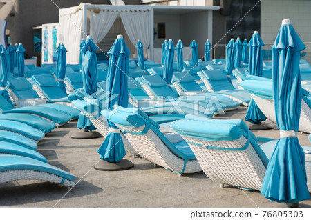 turquoise sun loungers and folded umbrellas in the background of the hotel, the concept of leisure turquoise sun loungers and folded umbrellas in the background of the hotel, the concept of leisure 76805303