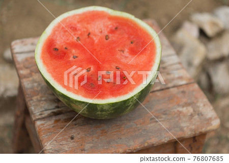 a ripe watermelon is cut and half a red watermelon lies on an old wooden stool, a rustic style, selective focusing a ripe watermelon is cut and half a red watermelon lies on an old wooden stool, a rustic style, selective focusing 76807685