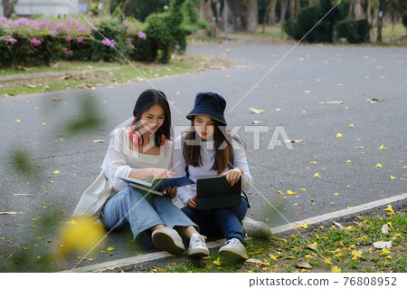 Two students are sitting in university during reading a book and communication. Study, education, university, college, graduate concept. Two students are sitting in university during reading a book and communication. Study, education, university, college, graduate concept. 76808952