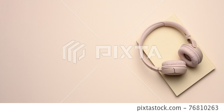 beige wireless headphones and a closed notepad on a beige background, banner 76810263