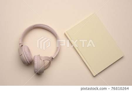 beige wireless headphones and a closed notepad on a beige background beige wireless headphones and a closed notepad on a beige background 76810264