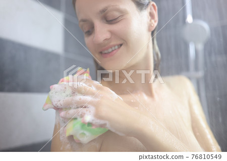 Young smiling woman washing herself with washcloth in shower Young smiling woman washing herself with washcloth in shower 76810549