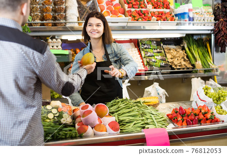 Female shopping assistant helping customer to buy fruit and vegetables in grocery shop 76812053