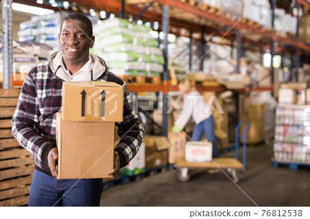 Smiling man carrying boxes in warehouse 76812538