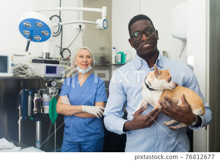 Happy african-american man holds her beloved dog chihuahua in her arms after being examined by a veterinarian Happy african-american man holds her beloved dog chihuahua in her arms after being examined by a veterinarian 76812677