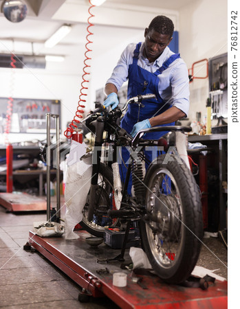 Service engineer repairing motorcycle in motorcycle service Service engineer repairing motorcycle in motorcycle service 76812742