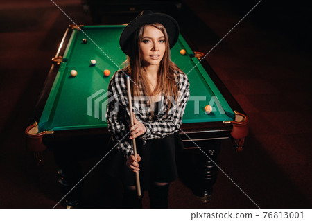 A girl in a hat in a billiard club with a cue in her hands.billiards Game A girl in a hat in a billiard club with a cue in her hands.billiards Game 76813001