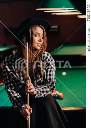 A girl in a hat in a billiard club with a cue in her hands.billiards Game A girl in a hat in a billiard club with a cue in her hands.billiards Game 76813002