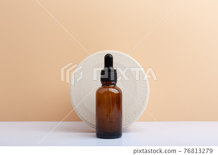 Skin serum in dark brown bottle against round stone circle on white table against beige background with copy space Skin serum in dark brown bottle against round stone circle on white table against beige background with copy space 76813279