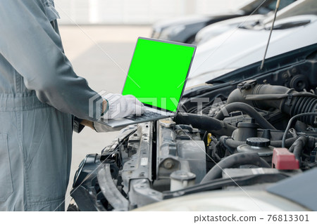 Mechanic using a laptop computer green screen to check collect information during work a car engine. service maintenance of industrial to engine repair. 76813301