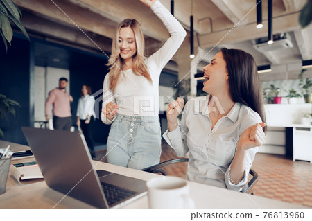 Two young happy businesswomen celebrating project success in office Two young happy businesswomen celebrating project success in office 76813960